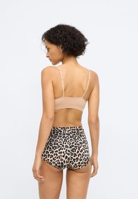 Bralette beige avec des bretelles réglables, associé à un short taille haute à motif léopard. Texture de tissu lisse.