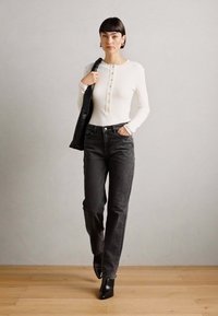 Haut à manches longues blanc léger et côtelé avec des boutons, associé à un jean droit gris foncé et des bottines noires. Textures lisses à travers l'ensemble.