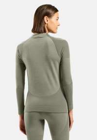 T-shirt thermique à manches longues, léger, de couleur olive avec un tissu texturé, un design ajusté et des accents côtelés le long des manches et du dos.