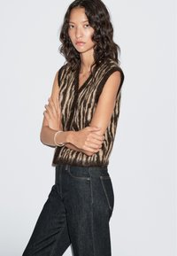 Gebreide mouwloze top met een V-hals, voorzien van een bruin en beige gestreept patroon. Combinatie met donkere spijkerbroek, met een soepele textuur en pasvorm.