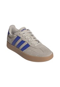 Sneaker in suede grigio con strisce in pelle blu, punta tonda, chiusura con lacci e suola in gomma beige. Presenta una texture liscia con accenti del logo.