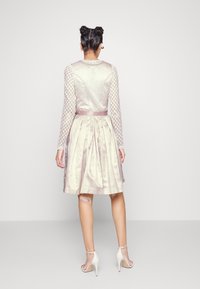 Une robe rose clair avec un tissu texturé et scintillant, de longues manches à motifs géométriques, un corsage ajusté, une jupe plissée et une ceinture en satin.