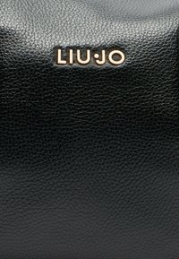 Melna teksturēta ādas soma ar zeltītu "LIU•JO" logotipu. Materiāls izceļas ar akmeņveida apdari un gludu virsmu.