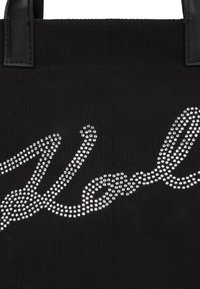 Fekete anyagú vámzsák, két fekete fogantyúval és ezüst strasszból készült kúrcíras felirattal az elején.