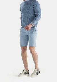 Shorts bleu clair à texture lisse, assortis à un pull bleu avec un ourlet et des poignets côtelés, et des baskets accentuées de gris.