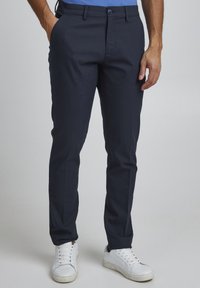 Chino blu navy realizzati in un tessuto di cotone resistente, caratterizzati da una vestibilità classica, tasche frontali e una chiusura con zip e bottone.