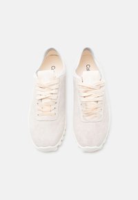 Paire de baskets en daim beige avec lacets plats et une étiquette logo sur fond blanc, vue de dessus.