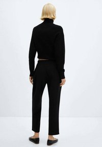 Sort cropped sweater med høj hals, kombineret med sorte lige bukser og flade sko, alle med en glat tekstur.