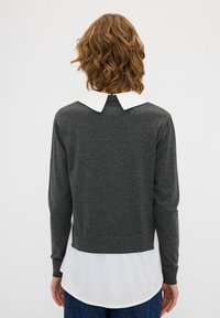 Grauer Pullover mit langen Ärmeln, cropped Design und weißem Peter-Pan-Kragen, kombiniert mit einem weißen Hemd, das darunter getragen wird.