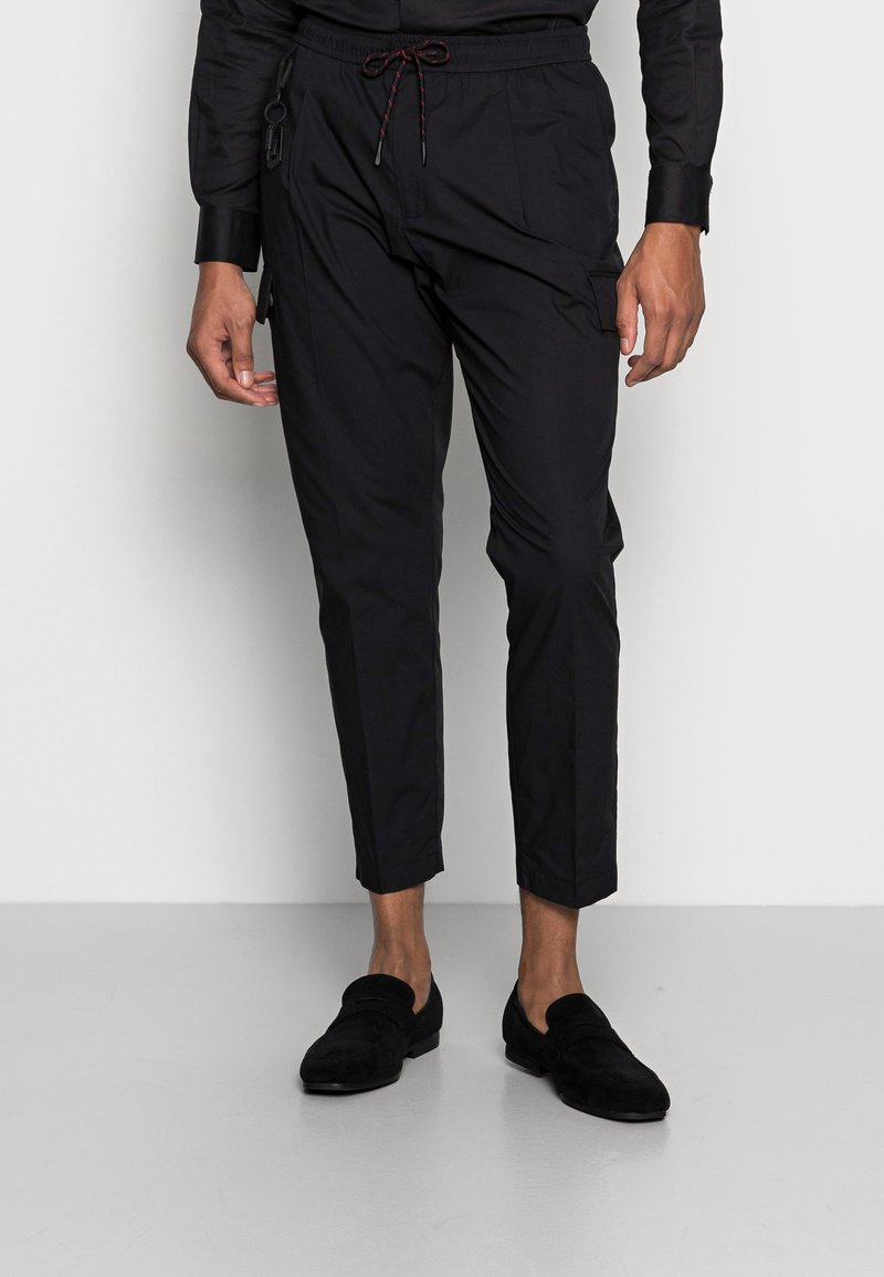 Pantalon noir fuselé en tissu léger avec une taille élastique et un cordon de serrage, doté de poches latérales et d'un design élégant.