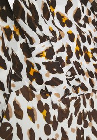 Biała koszula w panterkę w odcieniach brązu, beżu i żółci, z mankietami na guziki i widocznym przeszyciem.
