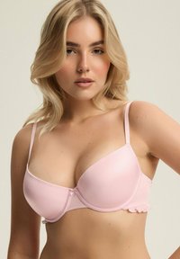Jasnoróżowy biustonosz z formowanymi miseczkami, cienkimi regulowanymi ramiączkami oraz falbaną na obwodzie, wykonany z gładkiego materiału.