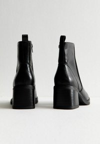 Zwarte leren enkellaarsjes met een ronde neus en een gestructureerde blokhak, voorzien van een lipje aan de achterkant en elastische zijkanten voor gemakkelijk aan- en uittrekken.