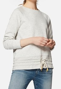 Sudadera gris claro con mangas raglán, dobladillo inferior fruncido y acento de cordón. Material suave de mezcla de algodón con una textura lisa.