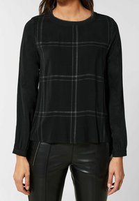 Svart långärmad topp med ett rutmönster i grått. Har en rund halsringning och något utsvängd nederkant, tillverkad av ett mjukt material.