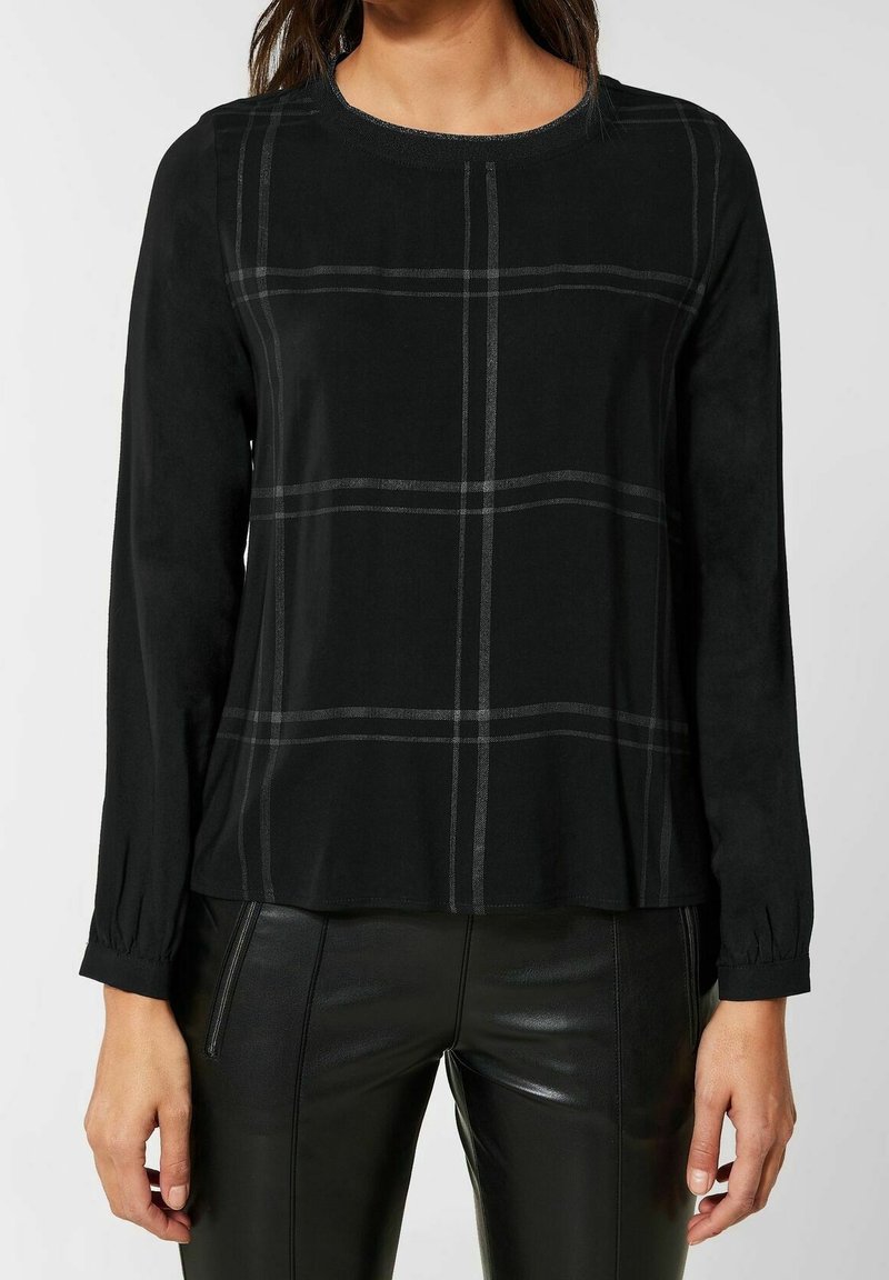 Svart långärmad topp med ett rutmönster i grått. Har en rund halsringning och något utsvängd nederkant, tillverkad av ett mjukt material.