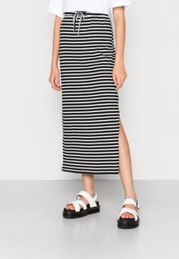 Pruhovaná černo-bílá maxi sukně se štěrbina, elastickým pasem s šňůrkou, spárovaná s bílými sandály s černou podešví.