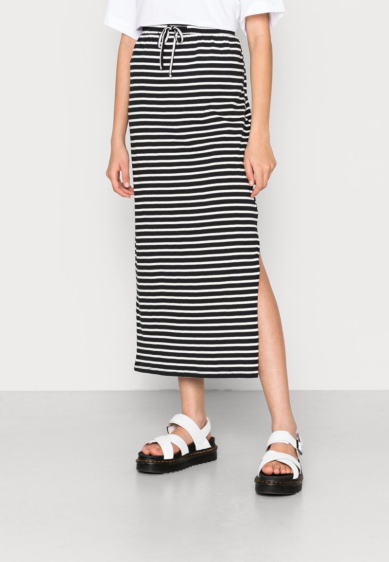 Pruhovaná černo-bílá maxi sukně se štěrbina, elastickým pasem s šňůrkou, spárovaná s bílými sandály s černou podešví.