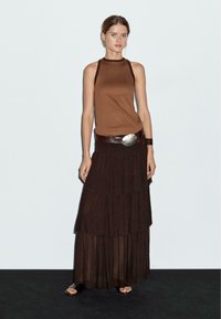 Brown sleeveless top paired with a layered dark brown maxi skirt. The outfit includes a wide, metallic-accented belt. Soft, flowing textures.