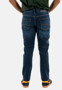 Jeans in denim blu scuro con taglio dritto, dotati di tasche posteriori con cuciture decorative e un'etichetta in pelle sulla vita.