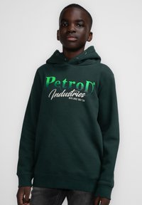 Tummanvihreä huppari, joka on valmistettu pehmeästä kankaasta ja jossa on rohkea "PetroD Industries" -logo vihreän ja valkoisen väriyhdistelmänä. Säädettävä naruhuppu.