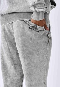 Pantalones de chándal grises elaborados con una tela suave y con una cintura acanalada. Presenta un bolsillo lateral, un corte ajustado y un logo negro en la cadera.