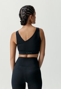 Čierny športový podprsenka s dizajnom V-chrbta, hrubými ramienkami a elastickým pásom s bielym logom. Legíny s vysokým pásom v rovnakom štýle.