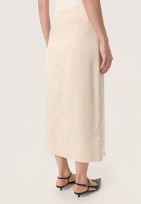 Gonna midi beige con taglio dritto, texture liscia e dettagli di cucitura sottili, abbinata a tacchi slingback neri.