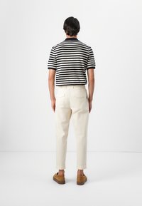 Polo de punto de manga corta con rayas en azul marino y blanco, combinado con pantalones de corte relajado de color claro y zapatos de ante marrón.
