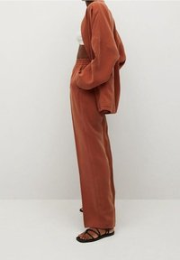 Przesadnie duża, rdzawoczerwona bluza i dopasowane zwężane spodnie z miękkiego materiału; posiada boczne kieszenie i elastyczny pas; zestawione z czarnymi sandałami.