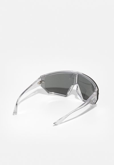 Clear, angular sunglasses with dark lenses and transparent frames. Features sleek, narrow arms and a minimalistic design.