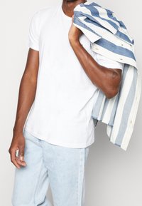 Vit t-shirt med kort ärm, kombinerad med ljusblå jeans. Bär en denimjacka med horisontella blå och vita ränder.