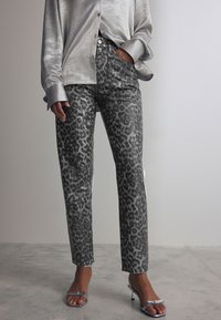 Jeans à imprimé léopard gris avec une coupe droite, associés à une chemise en satin gris clair avec fermeture à boutons et poignets larges.