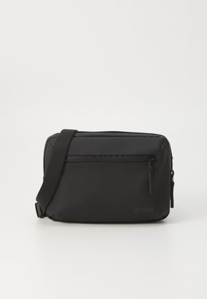 Sac en synthétique noir avec bandoulière réglable, poche zippée, et forme rectangulaire plate. Présente le logo sur le devant et une texture lisse.