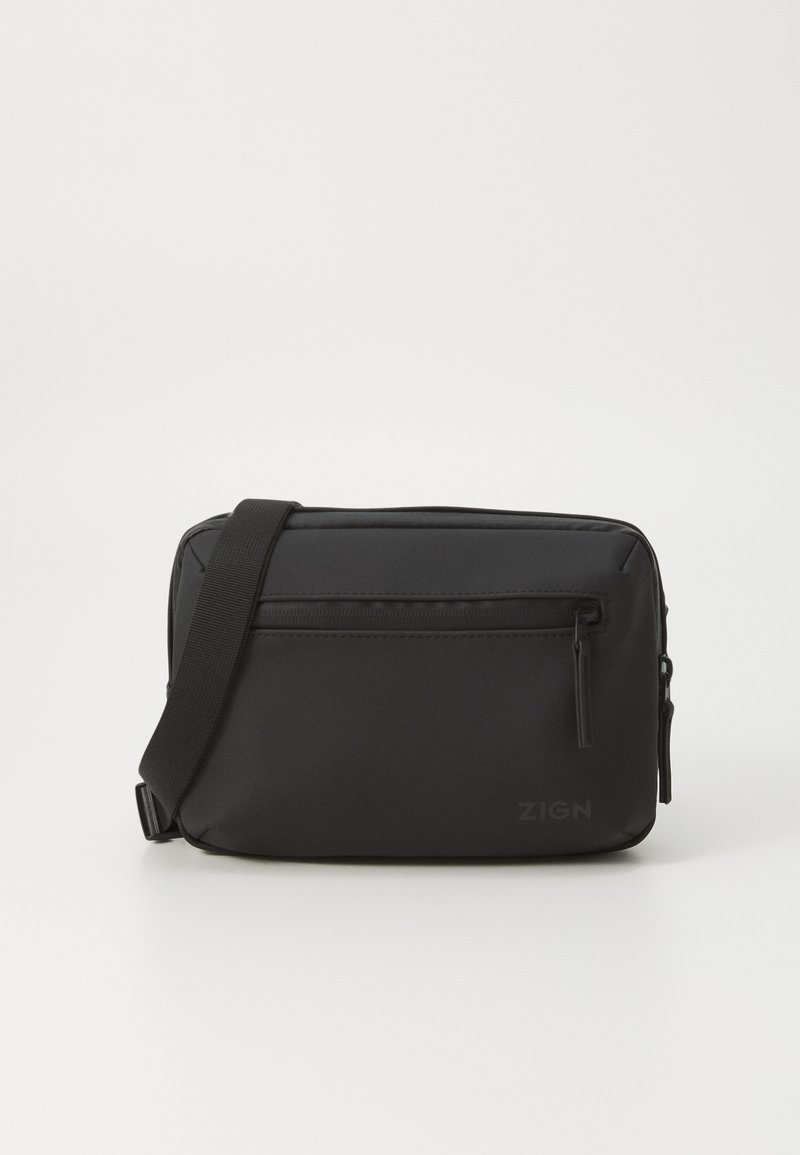 Sac en synthétique noir avec bandoulière réglable, poche zippée, et forme rectangulaire plate. Présente le logo sur le devant et une texture lisse.