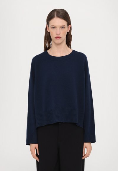 Navy blue neulepaita, jossa on pyöreä kaula-aukko, alhaalla laskeutuvat olkapäät ja ribbireunus. Kangas näyttää pehmeältä ja siinä on rento istuvuus.