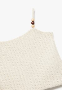 Paita puuvillasta off-white värissä, jossa on pystysuora röpelötekstuuri. Varustettu säädettävällä hihnalla, jossa on puuhelmiä sulkumekanismina.