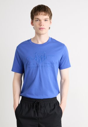 Blauwe katoenen t-shirt met een reliëflogo op de borst, ronde halslijn en korte mouwen. Gecombineerd met zwarte shorts met elastische tailleband.