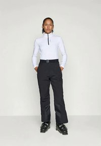 Λευκή μπλούζα με μακριά μανίκια και υψηλό γιακά, με μαύρο φερμουάρ, συνδυασμένη με μαύρο παντελόνι με ζώνη. Το μοντέλο φορά μαύρες μπότες σκι.