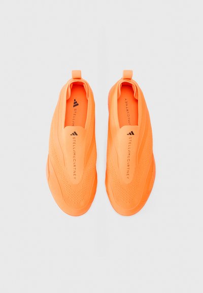 Lysende oransje slip-on joggesko med en teksturert strikket overdel og gummisåle. Har en merket logo på siden og en glatt, strømlinjeformet design.