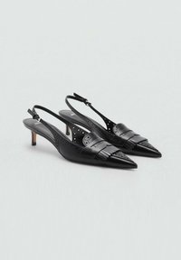 Décolleté in pelle nera con punta affusolata, dettagli decorativi a frange e perforazioni; presenta un tacco sottile.