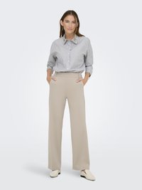 Un pantalon beige à jambes larges associé à une chemise boutonnée bleu et blanche à rayures, avec un col distinctif et des boutons proéminents.