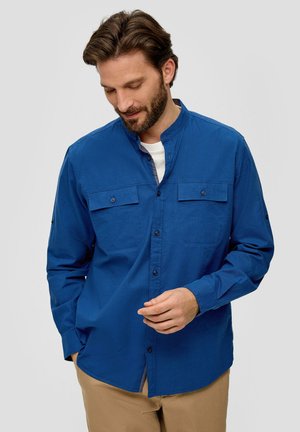 Blauwe overhemden met een mandarijnkraag, twee borstzakken en lange mouwen. Gewatteerde stof en een rechte zoom met een zijinsnijding.