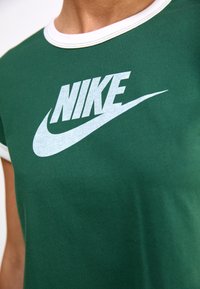 Green cotton t-shirt with a white crew neck and contrast stitching, featuring a large white Nike logo graphic on the front.
