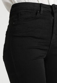 Jean noir taille haute en tissu mélangé de coton, avec une texture lisse, un design classique à 5 poches et de simples accents en métal.