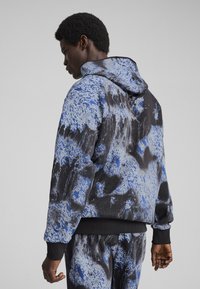 Sudadera con capucha en azul, negro y gris con un patrón salpicado. Presenta puños y dobladillo de canalé, y un tejido suave para mayor comodidad.