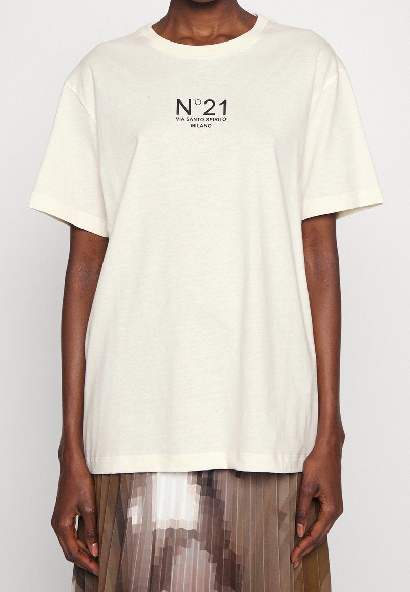 Camiseta de algodón color crema con mangas cortas, que presenta un diseño gráfico en negro: "N°21 VIA SANTO SPIRITO MILANO" en el centro.