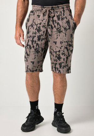Man draagt grijs-zwart abstract bedrukte knielange shorts met een trekkoord in de taille, zwarte sokken en zwarte sportschoenen.