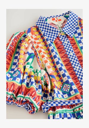 Kleurrijk patroon shirt met een blauwe geruite kraag, levendige rode, groene en gele designs, en opgezette mouwen met elastische manchetten.