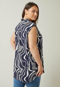 Marinblus utan ärmar med vitt vågmönster, rund halsringning och en lös passform. Tyget är lätt och har en mjuk textur.